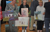 Trzy kobiety dumnie prezentujace obrazy w sali