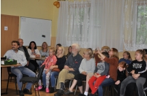 Grupa mlodszych i starszych osob siedzaca w sali