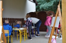 Dziewczynka malujaca obraz na sztaludze oraz dwoje chlopcow malujacych przy stolikach