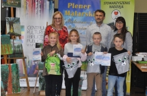 Dzieci trzymajace dyplomy i upominki na tle pozujacych z nimi doroslych