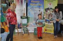 Dwie kobiety patrzace na chlopca prezentujacego obraz